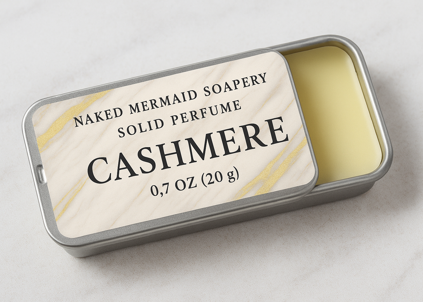Solid perfume in a tin labeled 'Cashmere' by Naked Mermaid Soapery on a light background