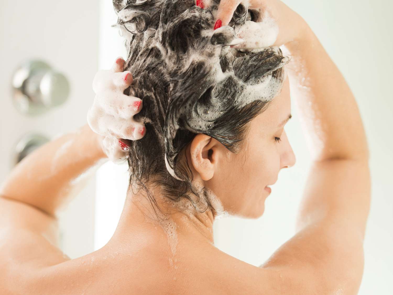 Woman washing hair with natural, sulfate-free shampoo in shower, enjoying clean beauty routine