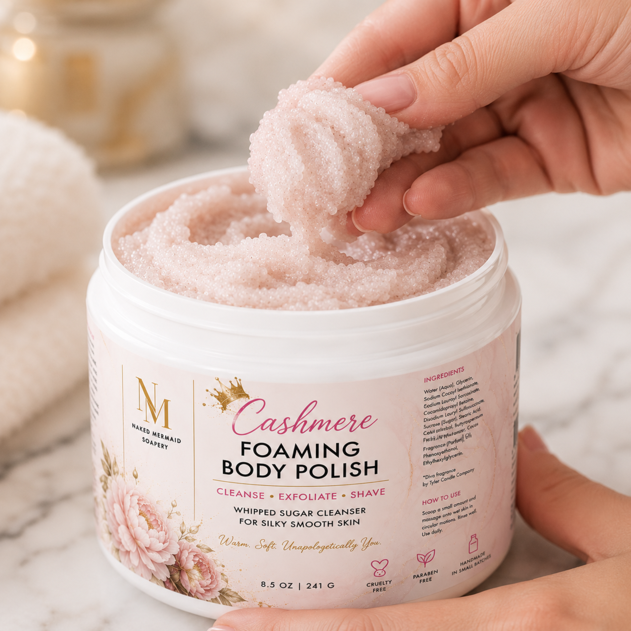 Hand scooping Cashmere Foaming Body Polish by Naked Mermaid Soapery from an 8.5 oz white jar, showcasing the luxurious whipped sugar texture designed to cleanse, exfoliate, and create a rich lather for silky smooth skin.
