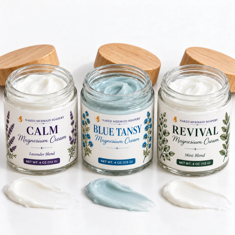 Three open 4 oz jars in the Botanical Magnesium Discovery Collection, showing white Calm and Revival creams and soft blue Blue Tansy cream, with matching swipes.
