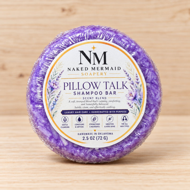 Pillow Talk shampoo bar by Naked Mermaid Soapery, a purple bar with a lavender floral label, standing upright on a light wood surface.