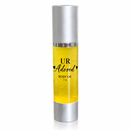 UR Adored 2 oz body oil in a clear airless pump bottle with silver cap and base, featuring a clear label with black text and filled with golden jojoba, amla, rosehip, and vitamin E oils on a clean white background.