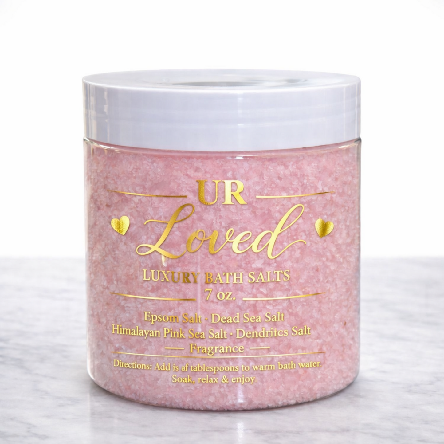 UR Loved luxury bath salts in a clear 7 oz jar with elegant gold foil label, featuring blush pink mineral salts displayed on a clean white marble surface.