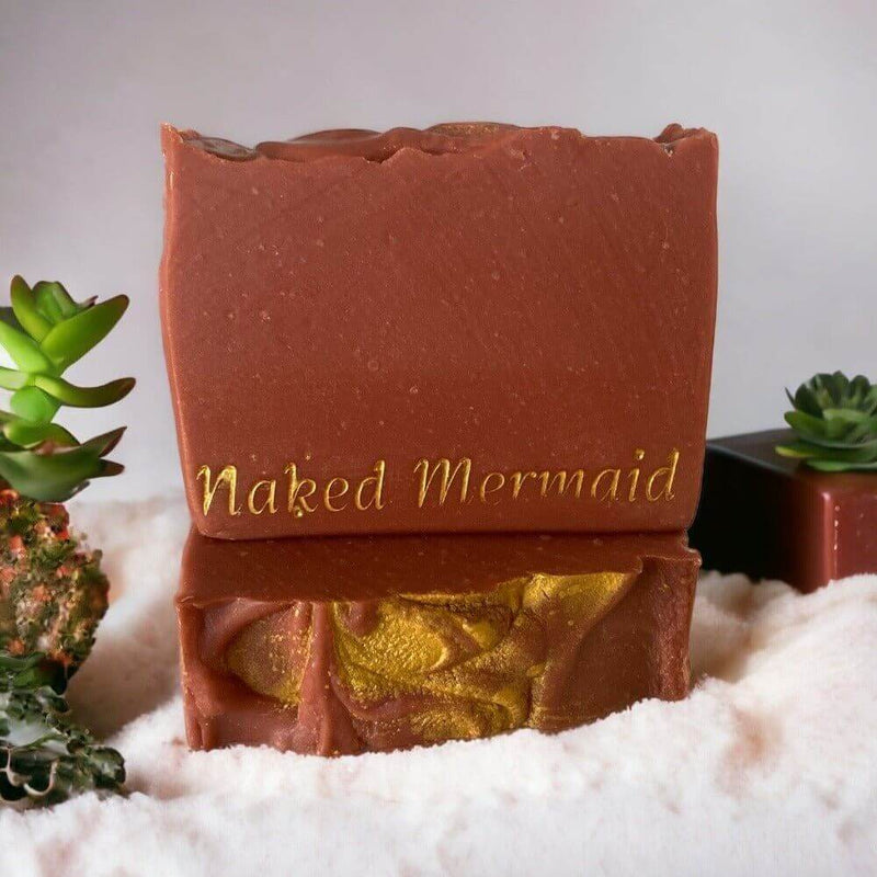 Handcrafted natural soap bar with gold swirls, 'Naked Mermaid' embossed, on sandy beach with succulents
