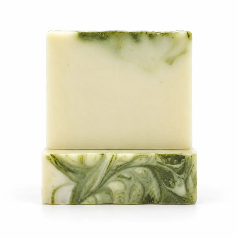 A handmade rectangular bar of soap with a light cream base and green marbled swirls, displayed on a matching green and cream soap block against a white background.